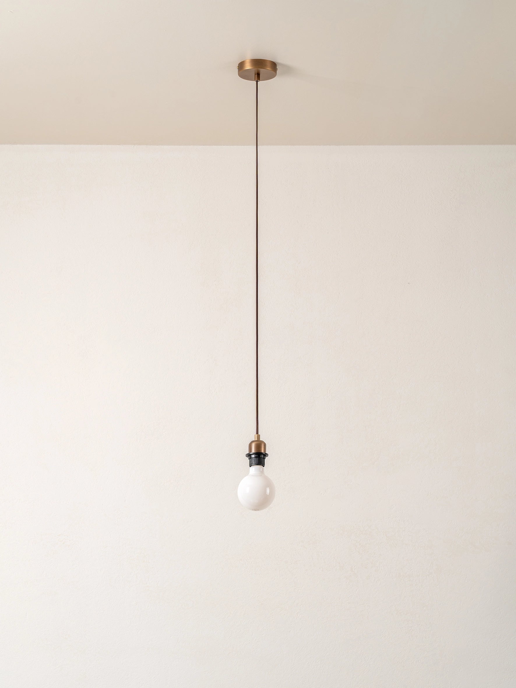Pendant light with a white bulb hanging against a plain wall.