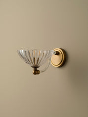 Wall-mounted light fixture with glass shade and gold finish on a beige wall