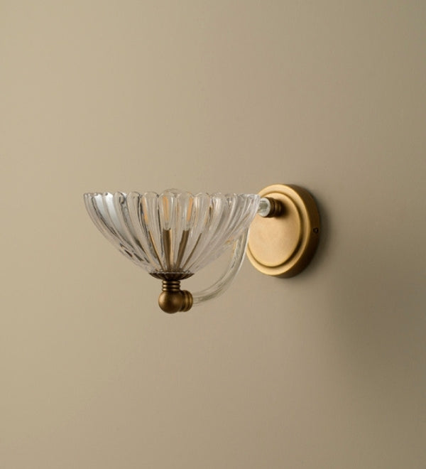 Wall-mounted light fixture with glass shade and gold finish on a beige wall