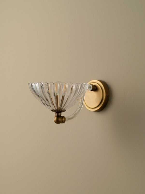 Wall-mounted light fixture with glass shade and gold finish on a beige wall