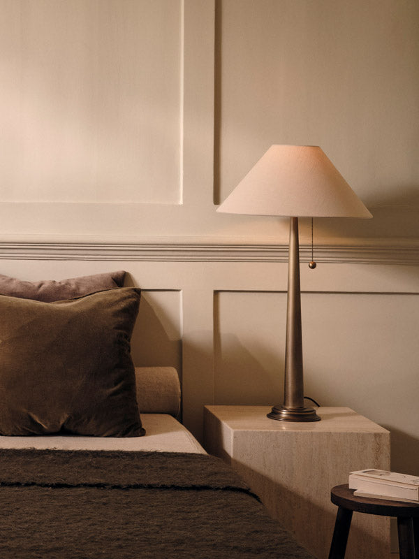 Table lamp on a side table next to a sofa with pillows in a cozy room.