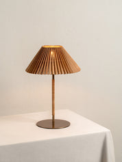 Table lamp with pleated brown shade on a white surface against a beige wall