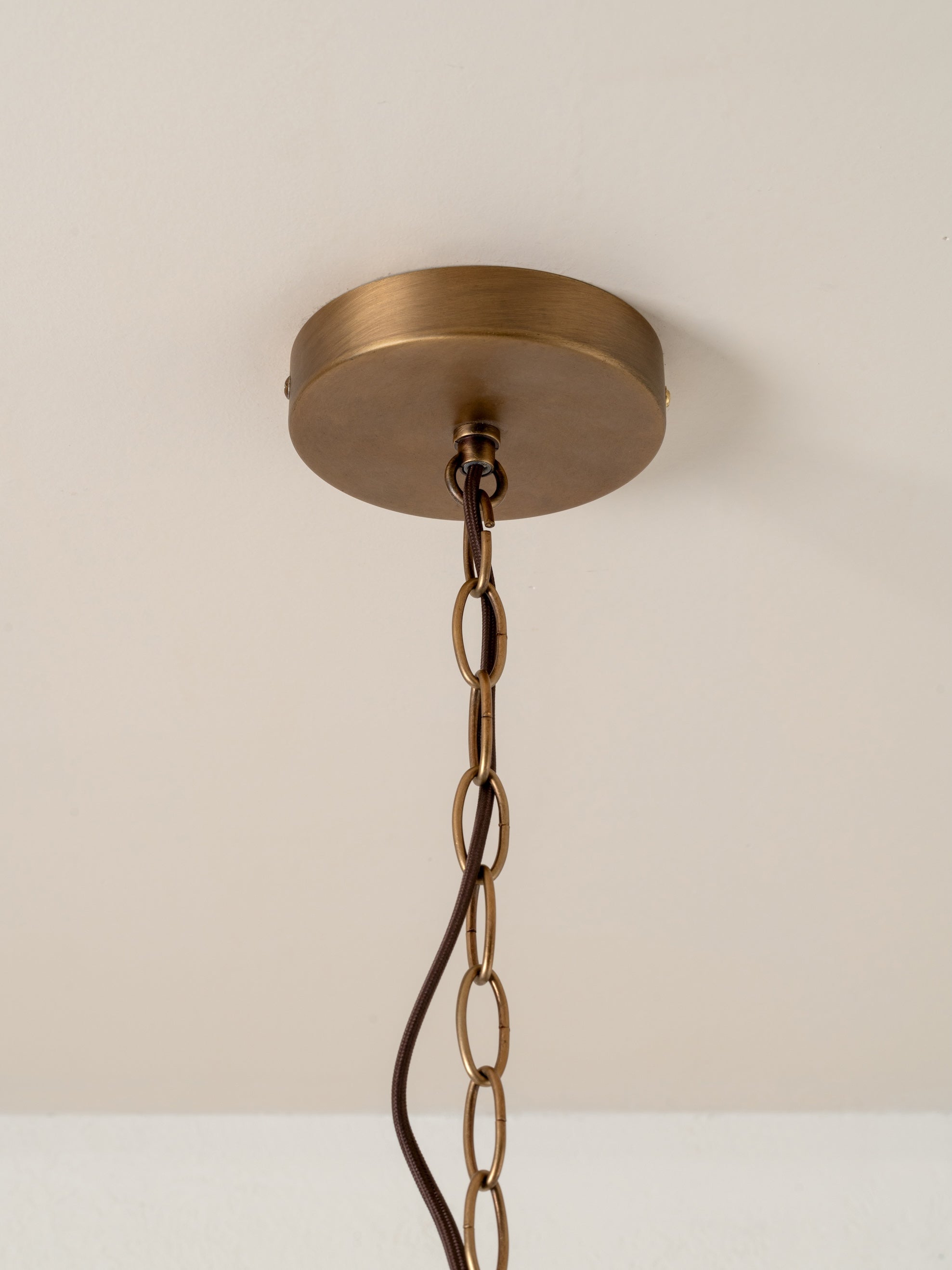 Brass ceiling light fixture with chain on a beige wall background