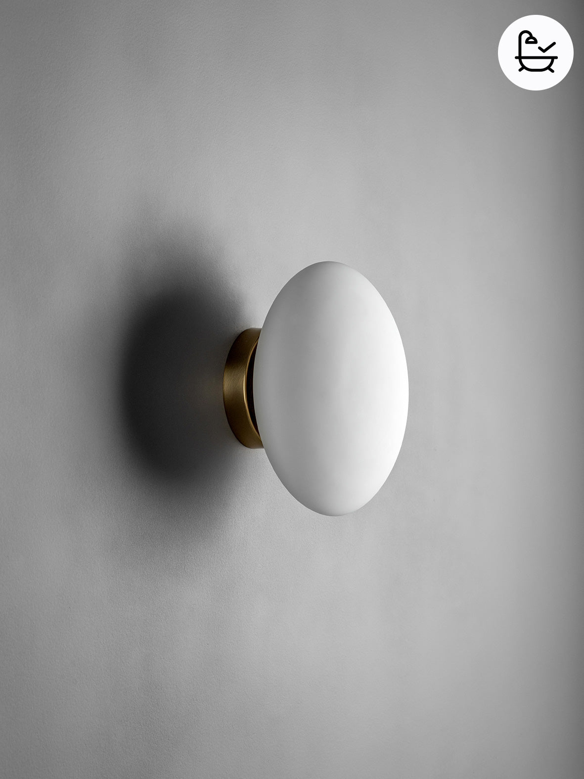 Wall-mounted light fixture with a white shade and gold base on a gray background