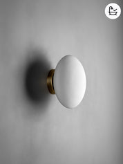 Wall-mounted light fixture with a white shade and gold base on a gray background