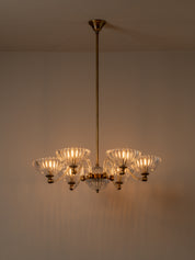 A six-light brass chandelier with clear ribbed glass shades, suspended from a ceiling against a neutral beige wall.