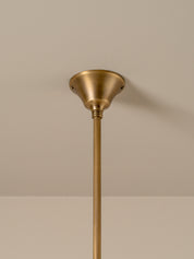 A close-up of a brass ceiling light fixture showing the round ceiling canopy and the top of the downrod against a neutral beige wall.