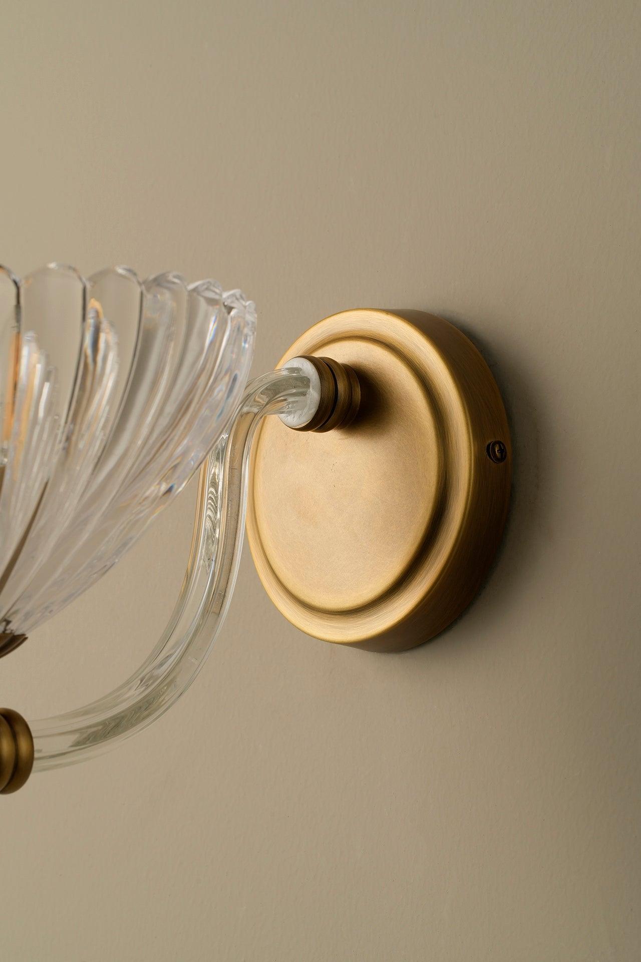 Wall-mounted light fixture with clear glass shade and brass finish on a beige wall.