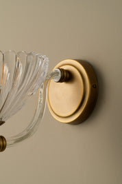 Wall-mounted light fixture with clear glass shade and brass finish on a beige wall.