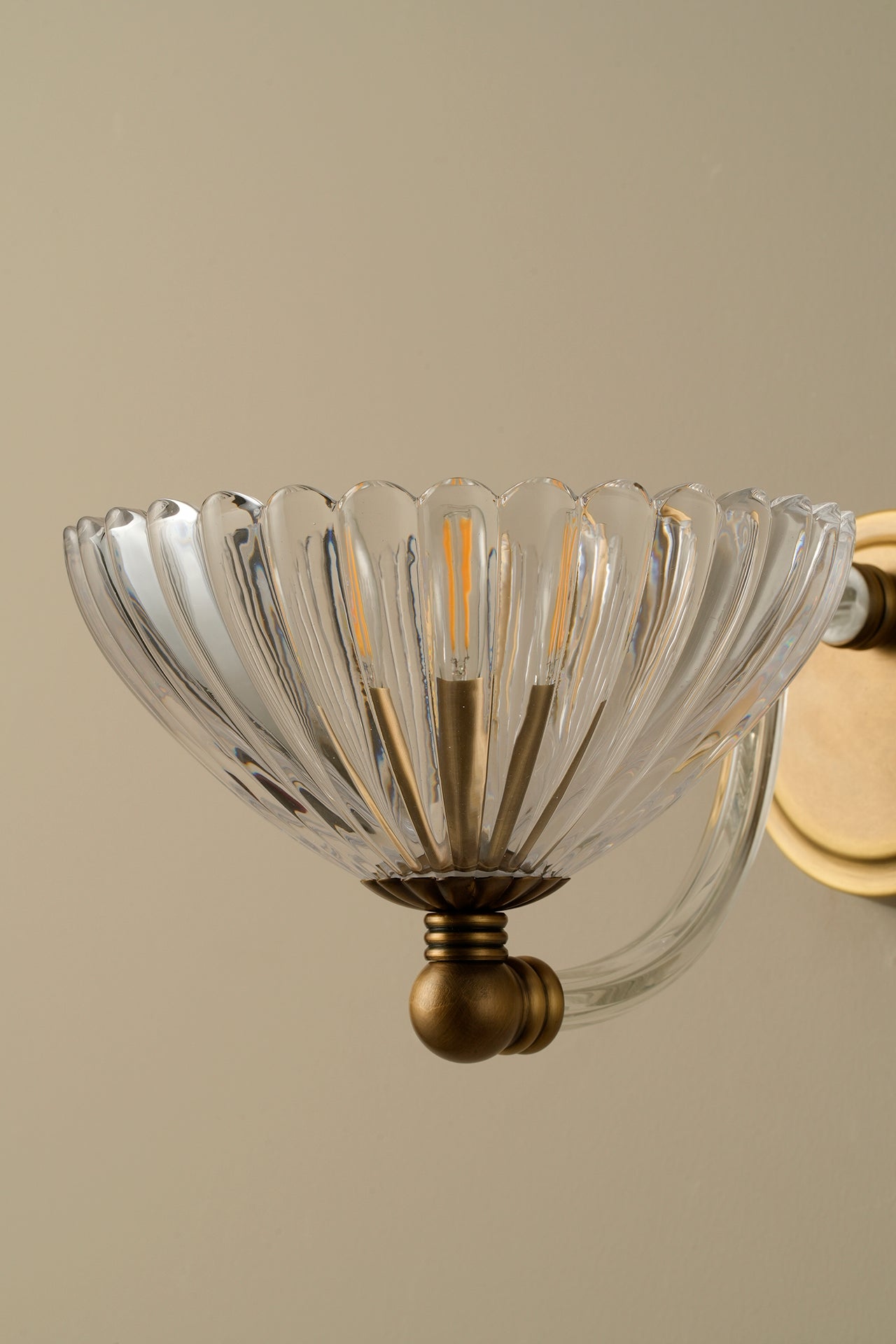 Decorative wall light fixture with clear glass shade and brass base on a beige background