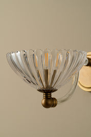 Decorative wall light fixture with clear glass shade and brass base on a beige background