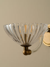 Clear glass wall sconce with gold metal fixture on a beige background