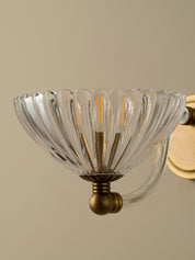 Clear glass wall sconce with gold metal fixture on a beige background