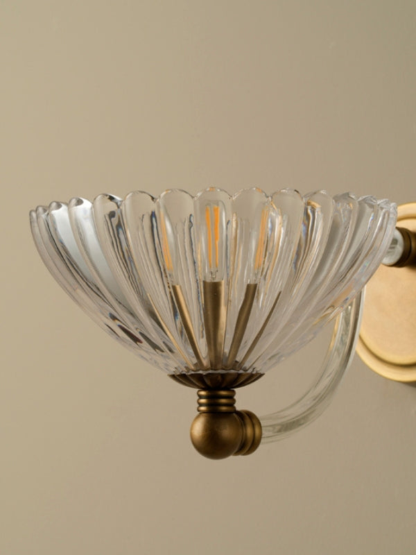 Clear glass wall sconce with gold metal fixture on a beige background