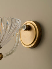 Wall-mounted light fixture with clear glass shade and gold metal base on a beige wall.