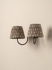 A two-light wall sconce with pleated fabric shades in a gray and beige pattern, mounted on a plain beige wall.