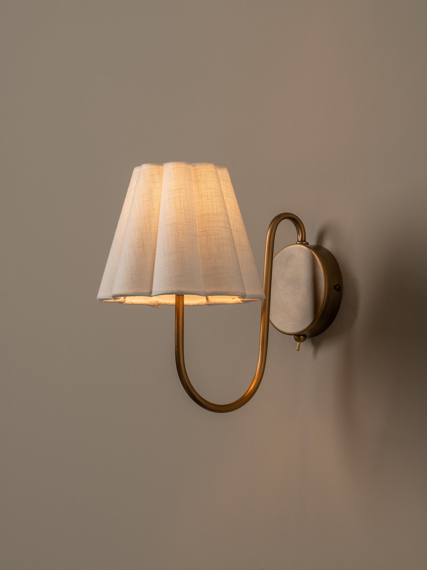 Wall-mounted lamp with a white shade and gold fixture on a plain wall.