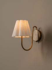Wall-mounted lamp with a white shade and gold fixture on a plain wall.