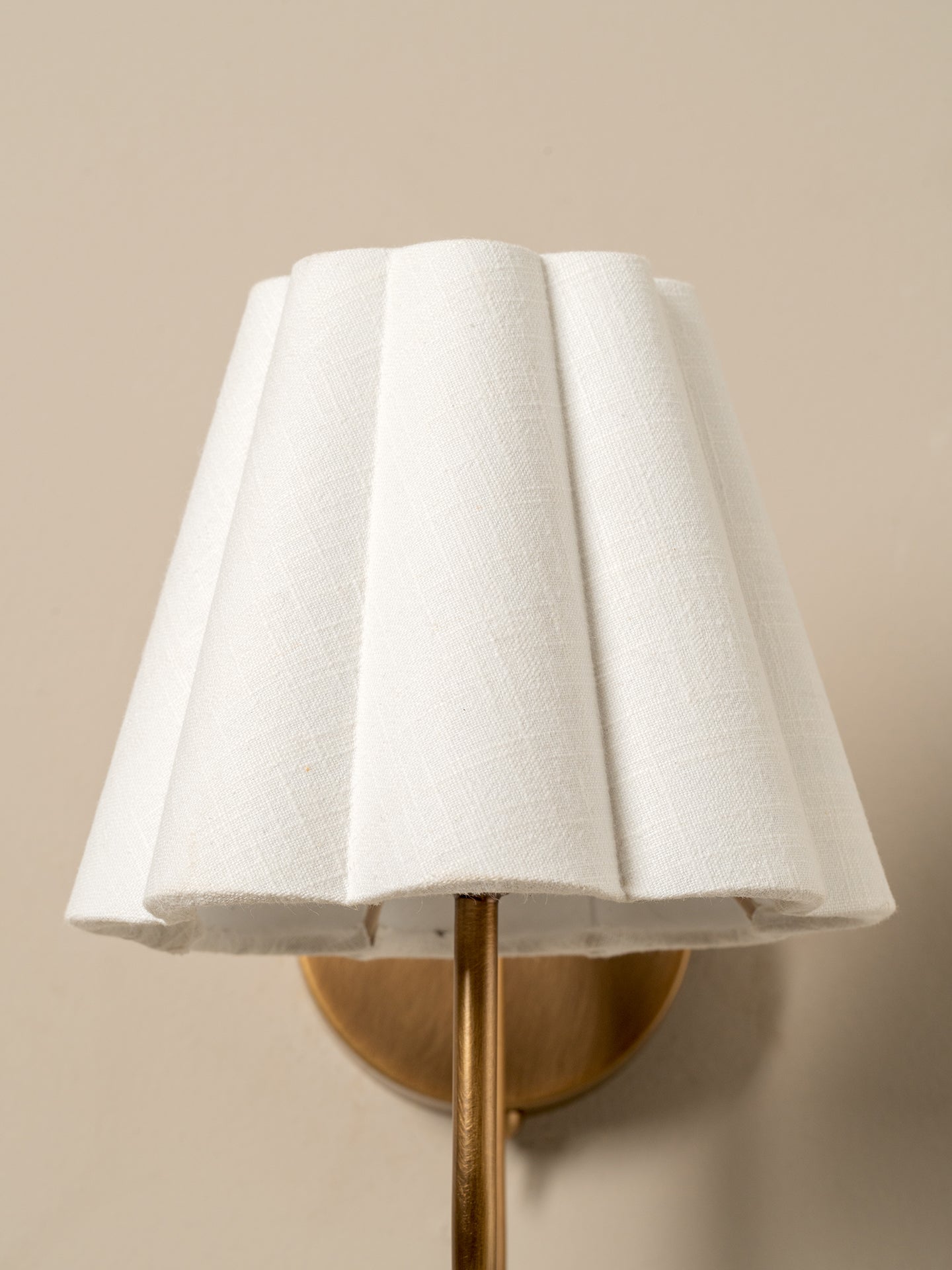 Wall-mounted lamp with a white shade and gold fixture on a beige wall.
