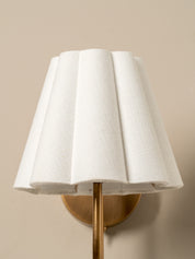 Wall-mounted lamp with a white shade and gold fixture on a beige wall.