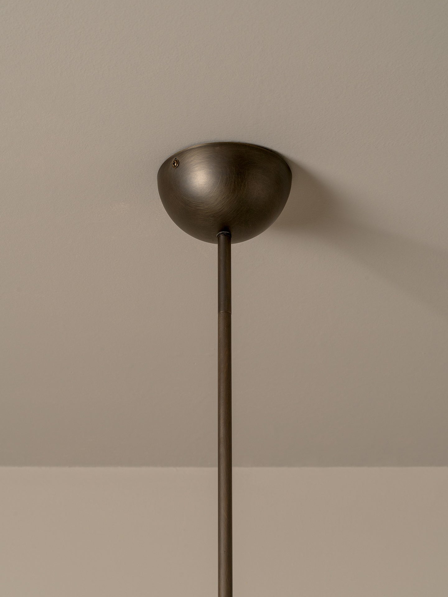 A close-up of a pendant light fixture showing its dome-shaped ceiling canopy and a long cylindrical rod against a neutral beige wall.