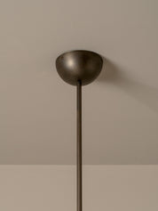 A close-up of a pendant light fixture showing its dome-shaped ceiling canopy and a long cylindrical rod against a neutral beige wall.