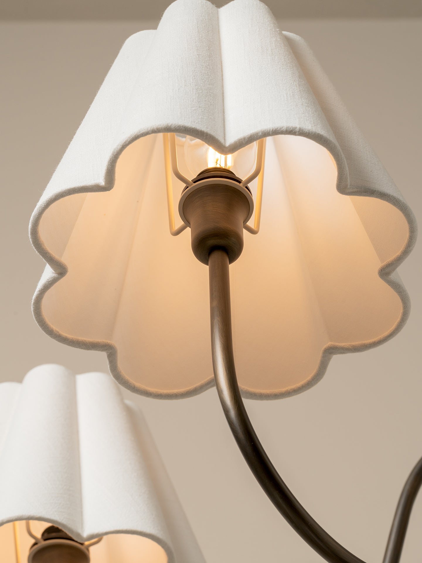 Close-up of a modern wall sconce with a warm white scalloped fabric shade and a dark bronze metal arm, glowing with an exposed bulb.