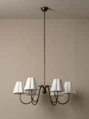 A six-light chandelier with white tapered fabric shades and a dark metal frame, suspended from a ceiling against a beige wall.