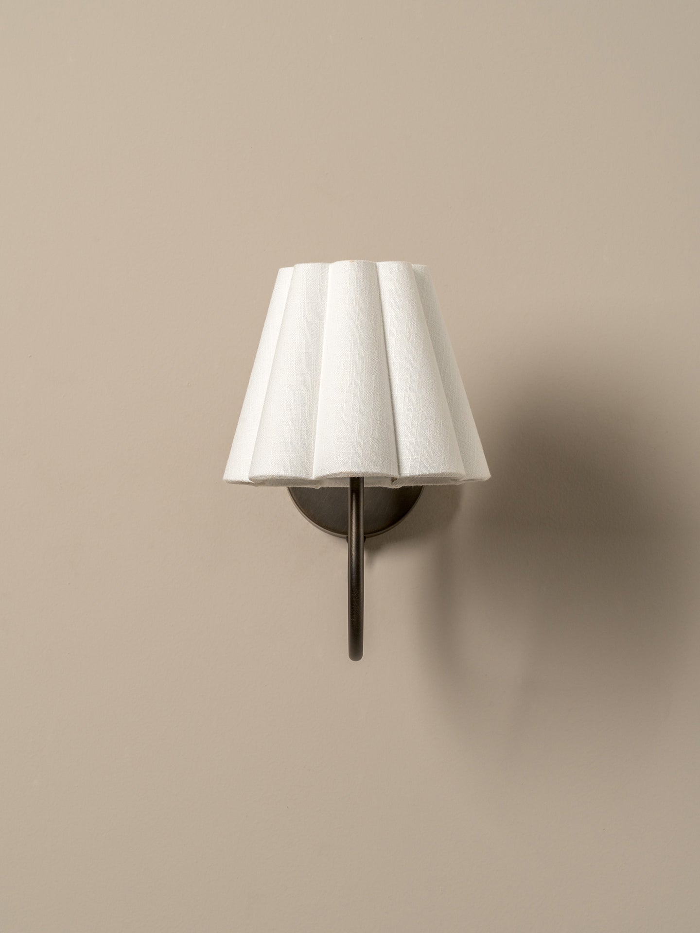 Wall-mounted lamp with a white pleated shade on a beige wall