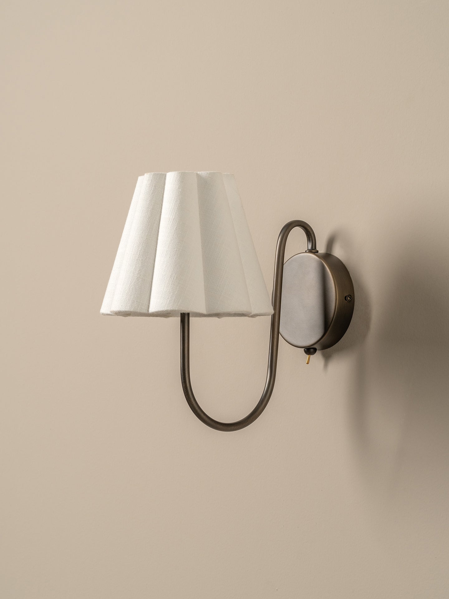 Wall-mounted lamp with a white shade and bronze fixture on a beige wall.