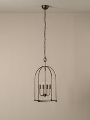 A dark metal birdcage pendant chandelier with five candle-style bulbs, suspended from a ceiling by a chain against a plain beige wall.