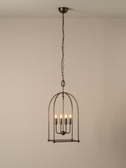 A dark metal birdcage pendant chandelier with five candle-style bulbs, suspended from a ceiling by a chain against a plain beige wall.