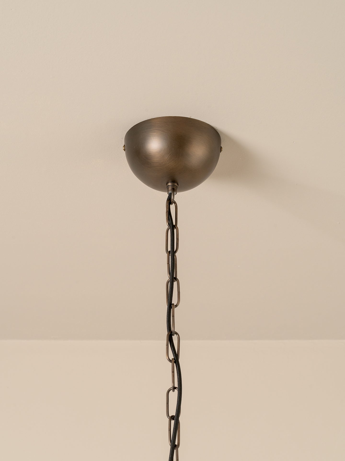 A dome-shaped ceiling mount with a dark bronze finish and a matching dark metal chain, shown against a plain beige wall and ceiling.