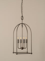 A dark metal cage pendant light fixture with four exposed filament bulbs, suspended by a chain against a plain beige background.