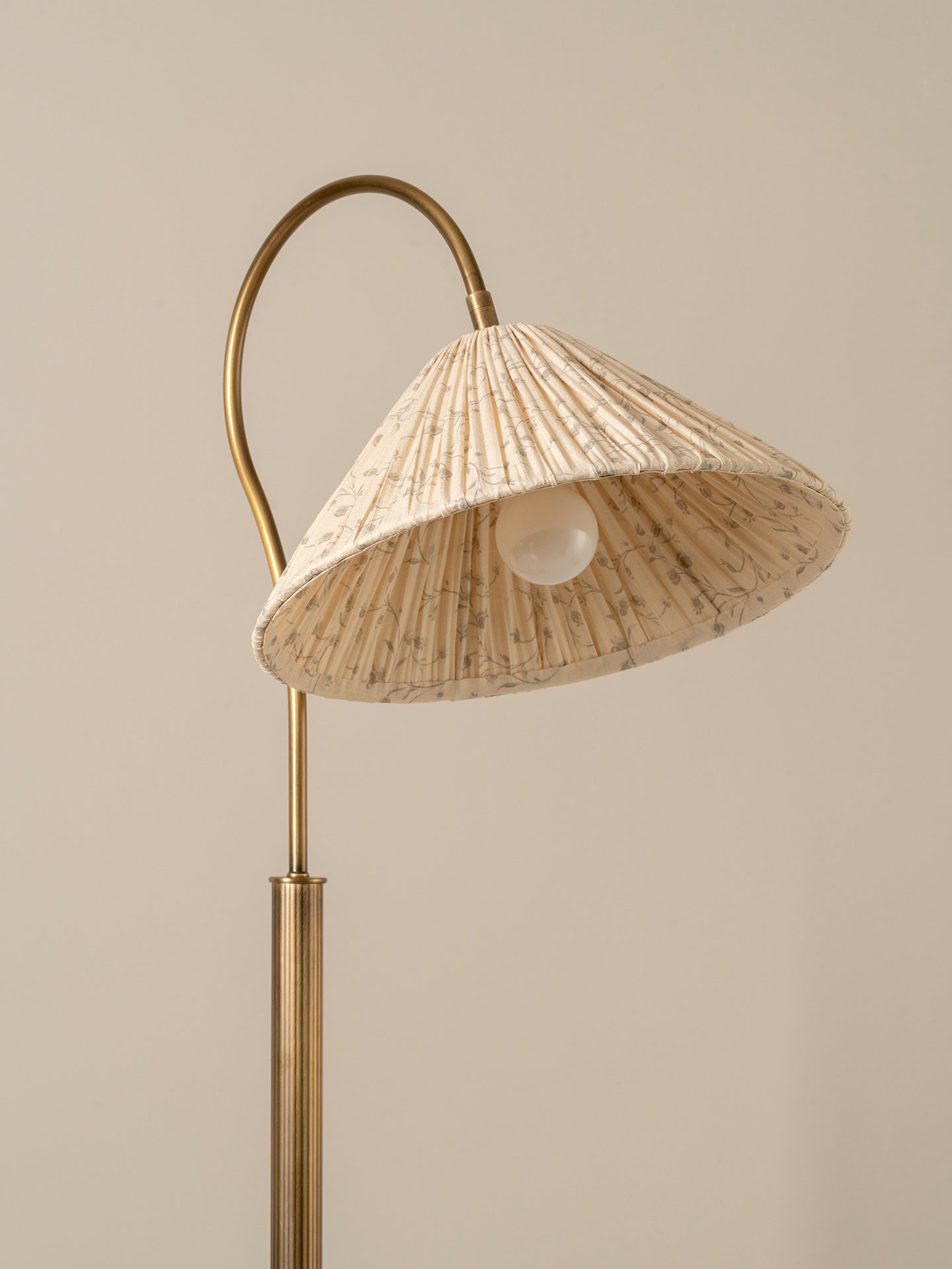 A modern floor lamp with a curved brass metal frame and a textured beige woven shade, shown against a solid warm beige background.