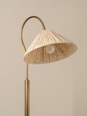 A modern floor lamp with a curved brass metal frame and a textured beige woven shade, shown against a solid warm beige background.
