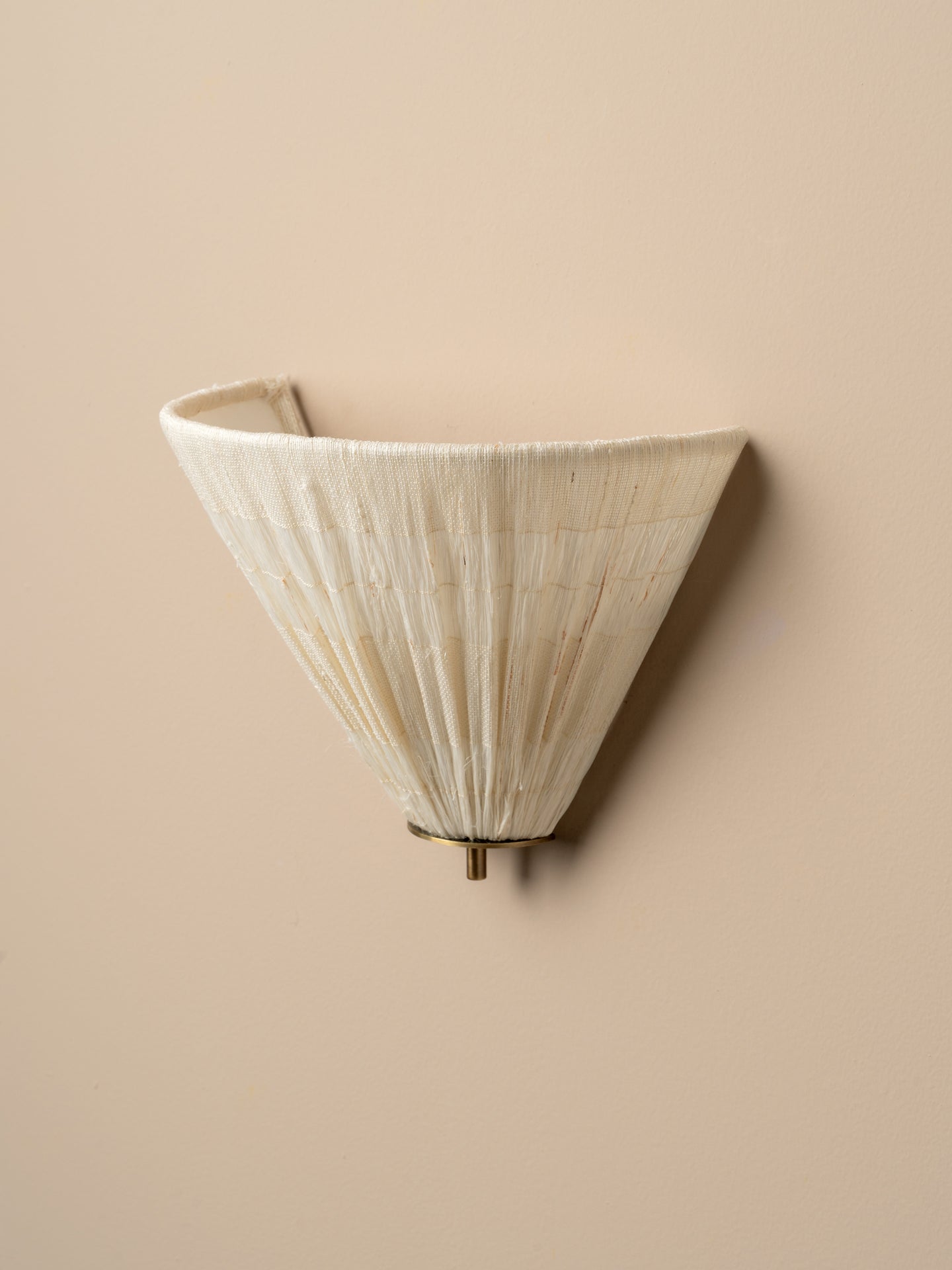 A modern wall sconce with a pleated, cone-shaped shade in a warm off-white or cream tone, mounted on a solid beige wall.