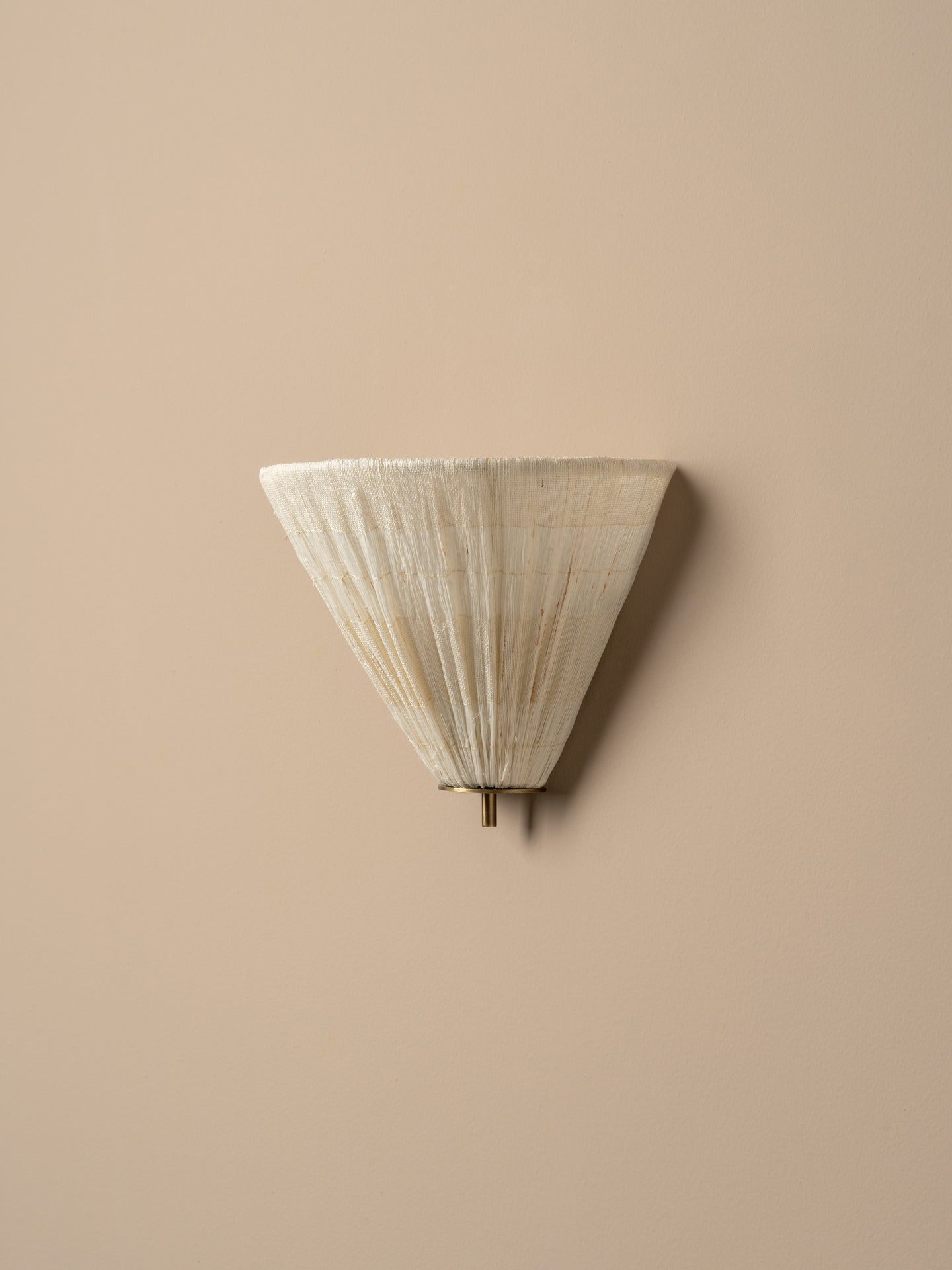 A modern wall sconce with a pleated, cone-shaped shade in a warm off-white or cream tone, mounted on a solid beige wall.