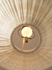 A close-up, upward view of a ceiling light fixture installed in a circular opening, showing a warm glowing globe bulb and brass-toned metal arms set against a textured beige radial ceiling surface.