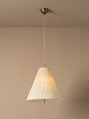 A close-up of a warm white textured fabric drum lampshade with a visible brass socket and glowing bulb inside, set against a solid warm beige background.