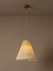 A conical pendant light shade made of textured, pleated cream-colored paper or fabric, suspended by a thin cord against a solid warm beige background. light is on.