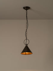 A dark metal pendant light with a conical shade and warm glowing interior, hanging from a chain against a plain beige wall and ceiling.