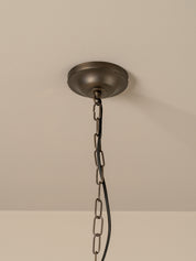 An industrial ceiling light fixture with a round, dark bronze ceiling canopy hanging from a heavy metal chain against a plain off-white wall.