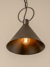 A dark metal cone pendant light with a warm glowing Edison bulb inside, hanging against a plain beige wall.