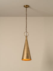A single brass pendant light with a conical shade hanging from a chain and ceiling canopy against a plain beige wall.