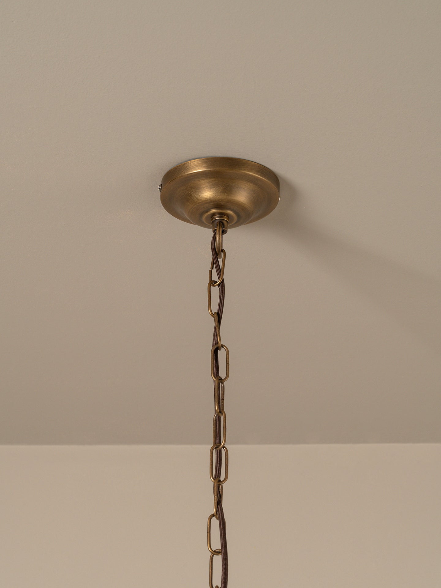An antique brass ceiling light fixture canopy and hanging chain, shown against a neutral beige wall and ceiling.
