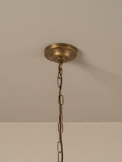 An antique brass ceiling light fixture canopy and hanging chain, shown against a neutral beige wall and ceiling.