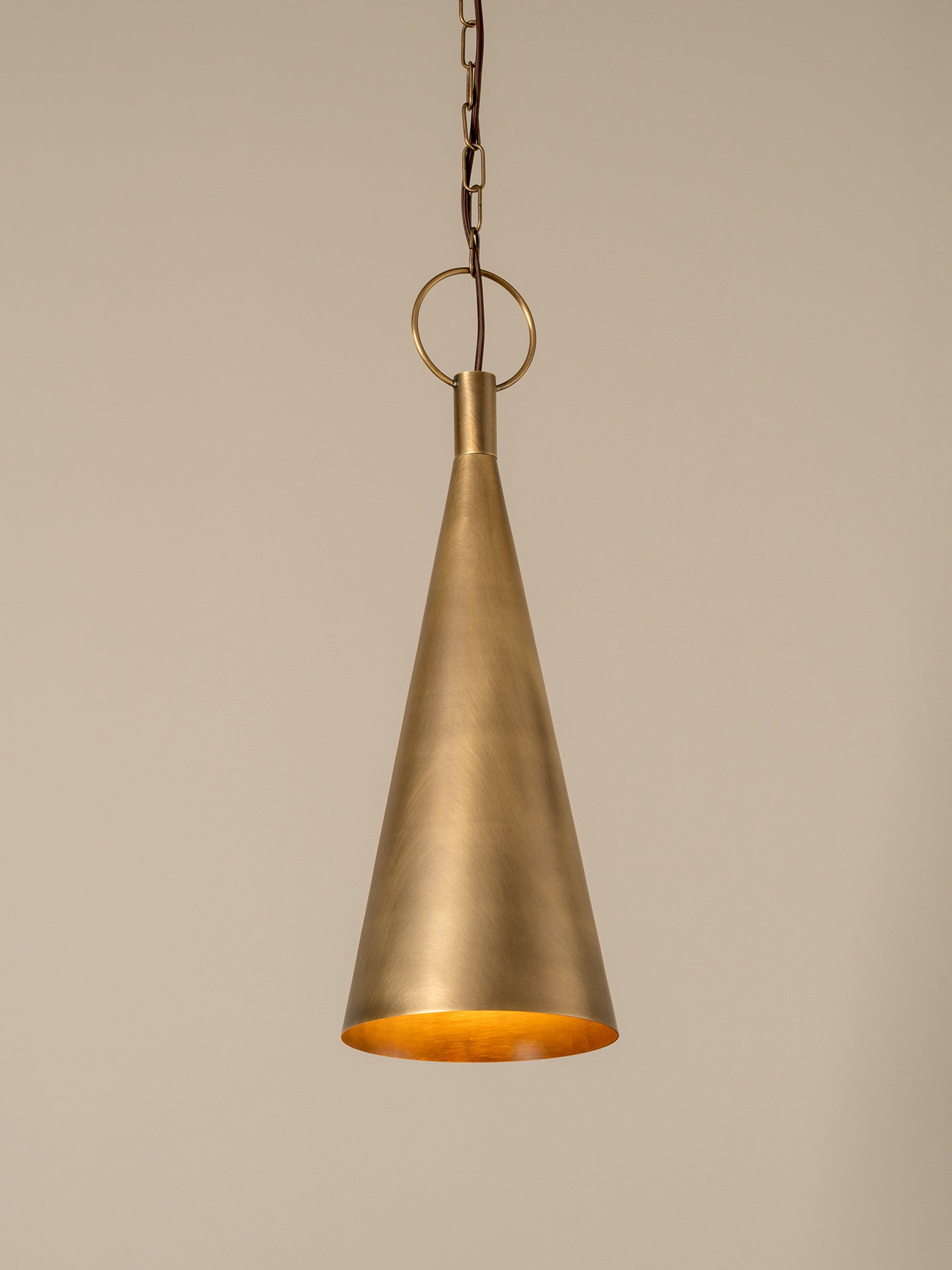 A hanging pendant light with a brushed brass or bronze metal shade and a matching chain, shown against a plain warm beige background.