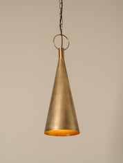 A hanging pendant light with a brushed brass or bronze metal shade and a matching chain, shown against a plain warm beige background.