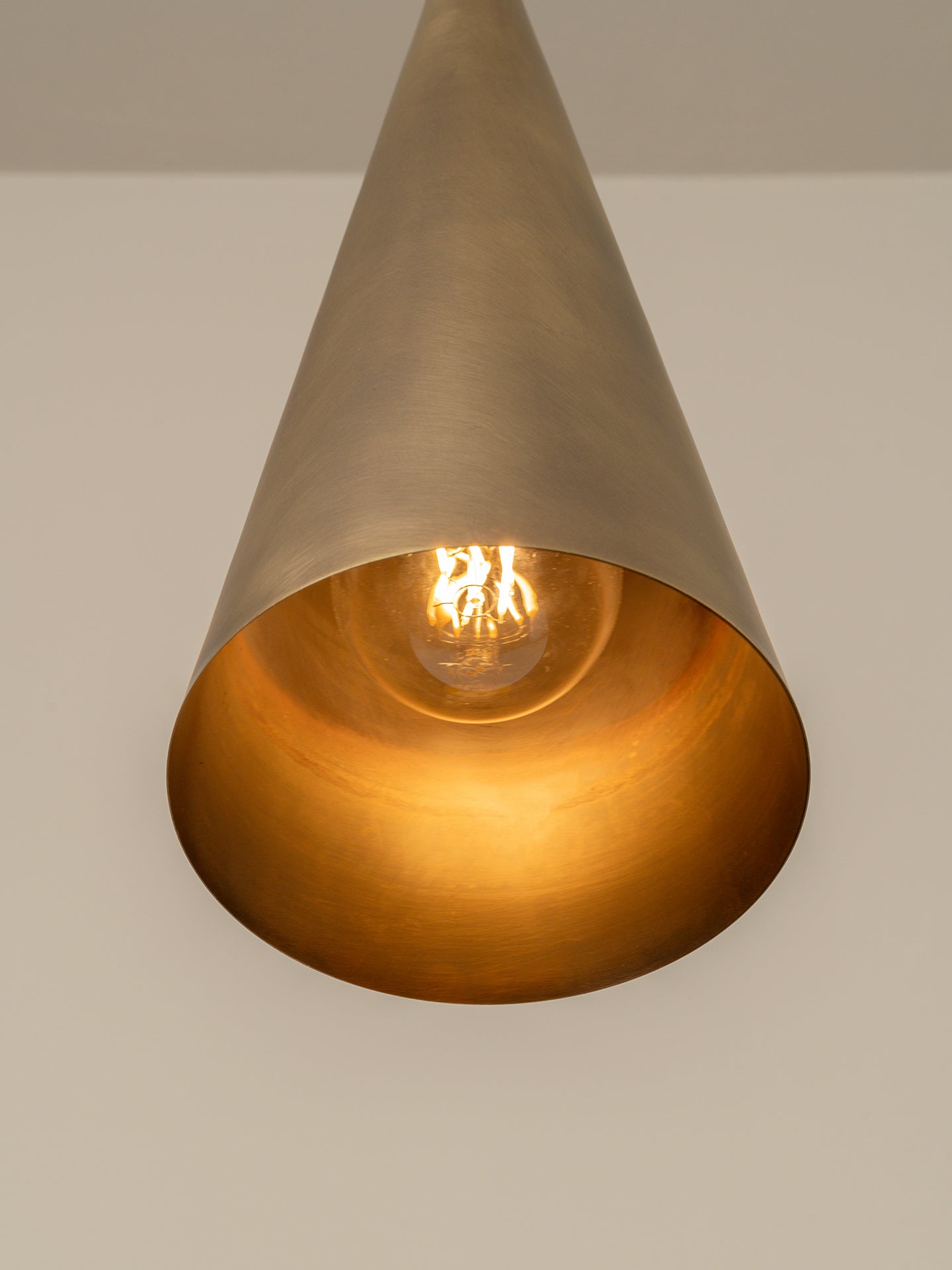 A cone-shaped pendant light fixture with a brushed brass exterior and a warm gold interior, illuminated with a visible Edison bulb.